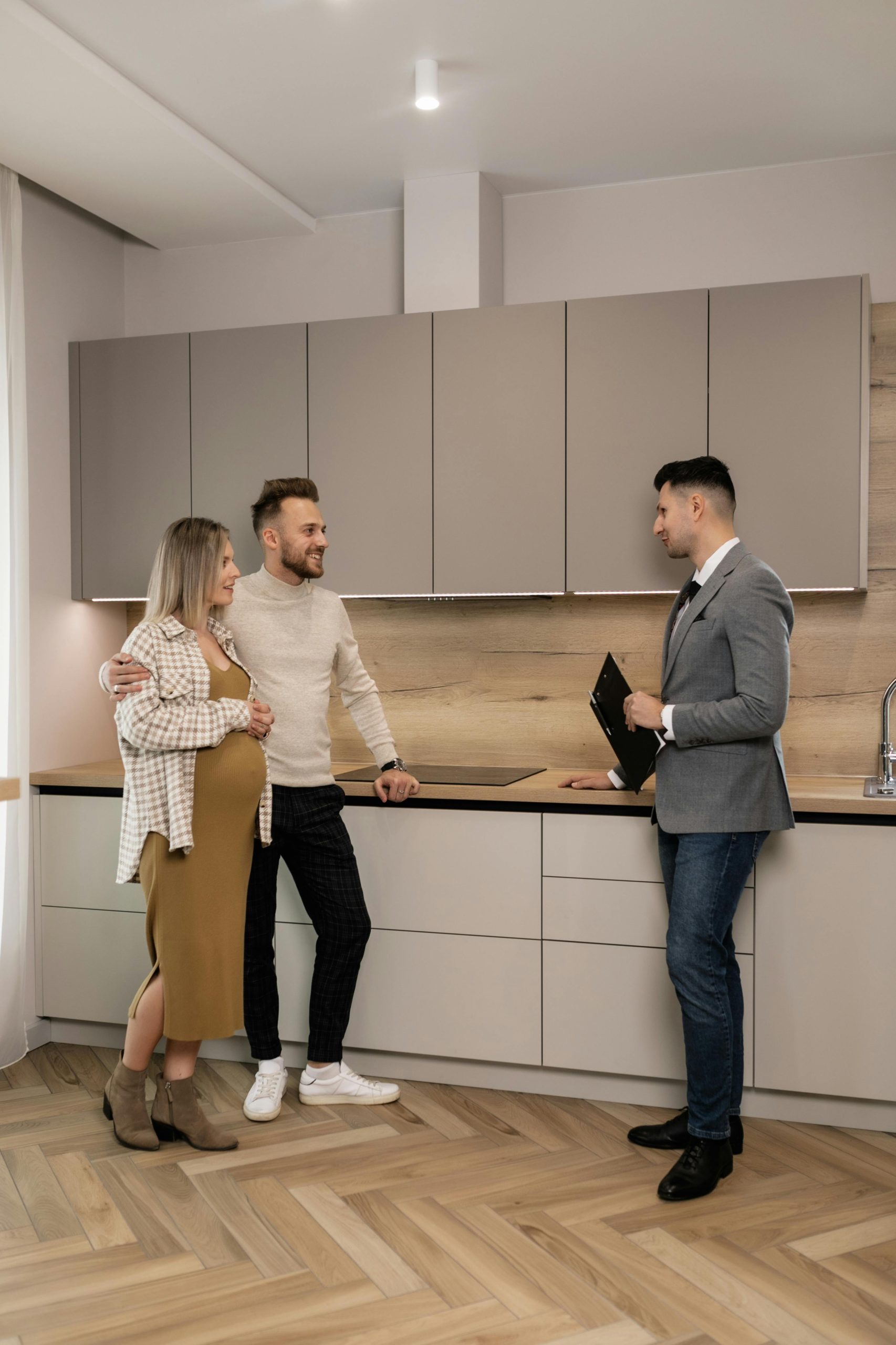 Pregnant couple joyfully discussing their future home purchase with a real estate agent in a modern kitchen.